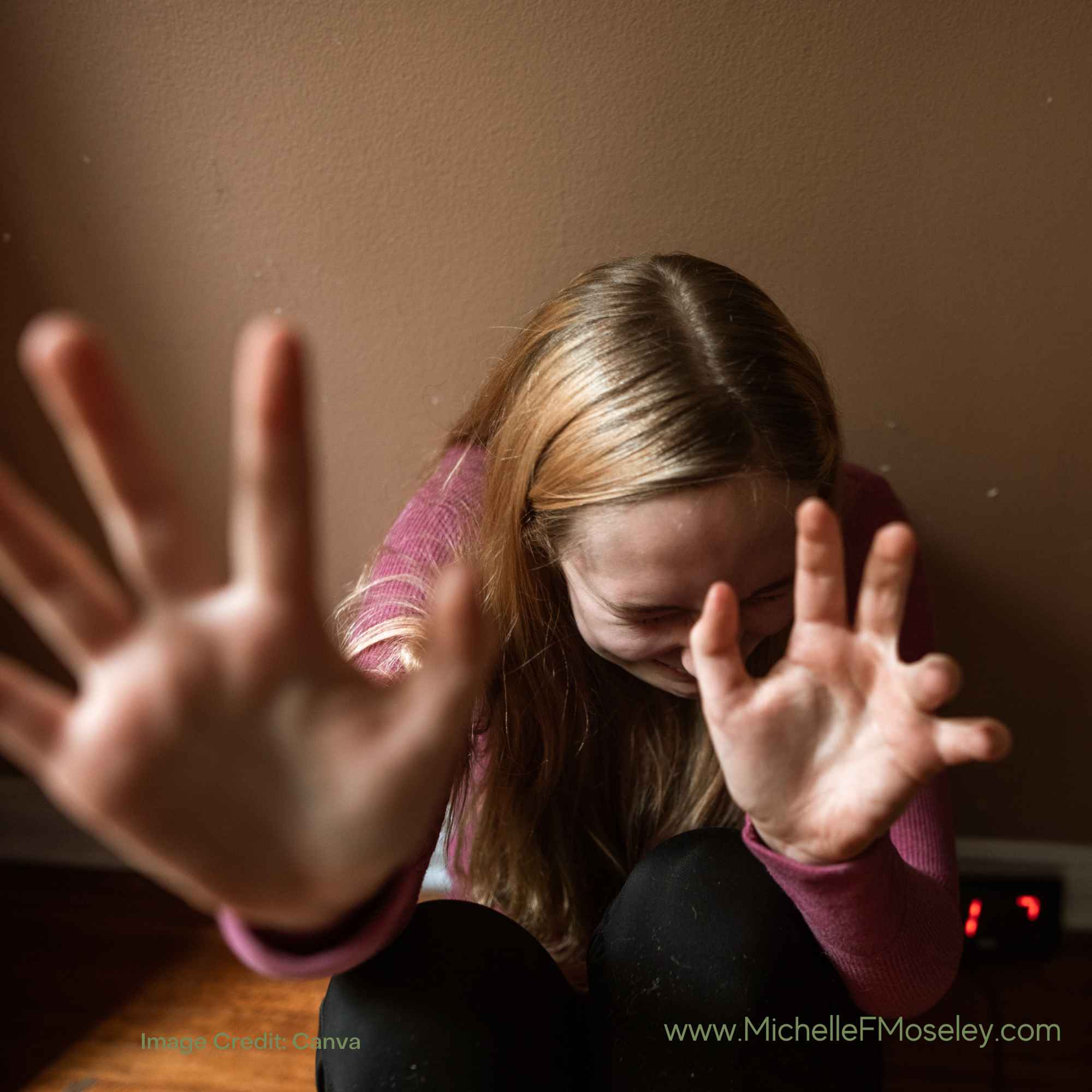 A woman seated on the floor pushing away someone or something with her hands.